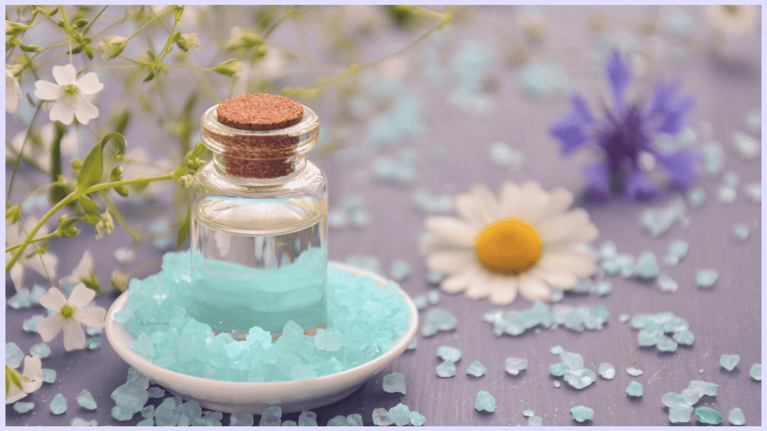 A vial of essential oil with crystals and flowers.
